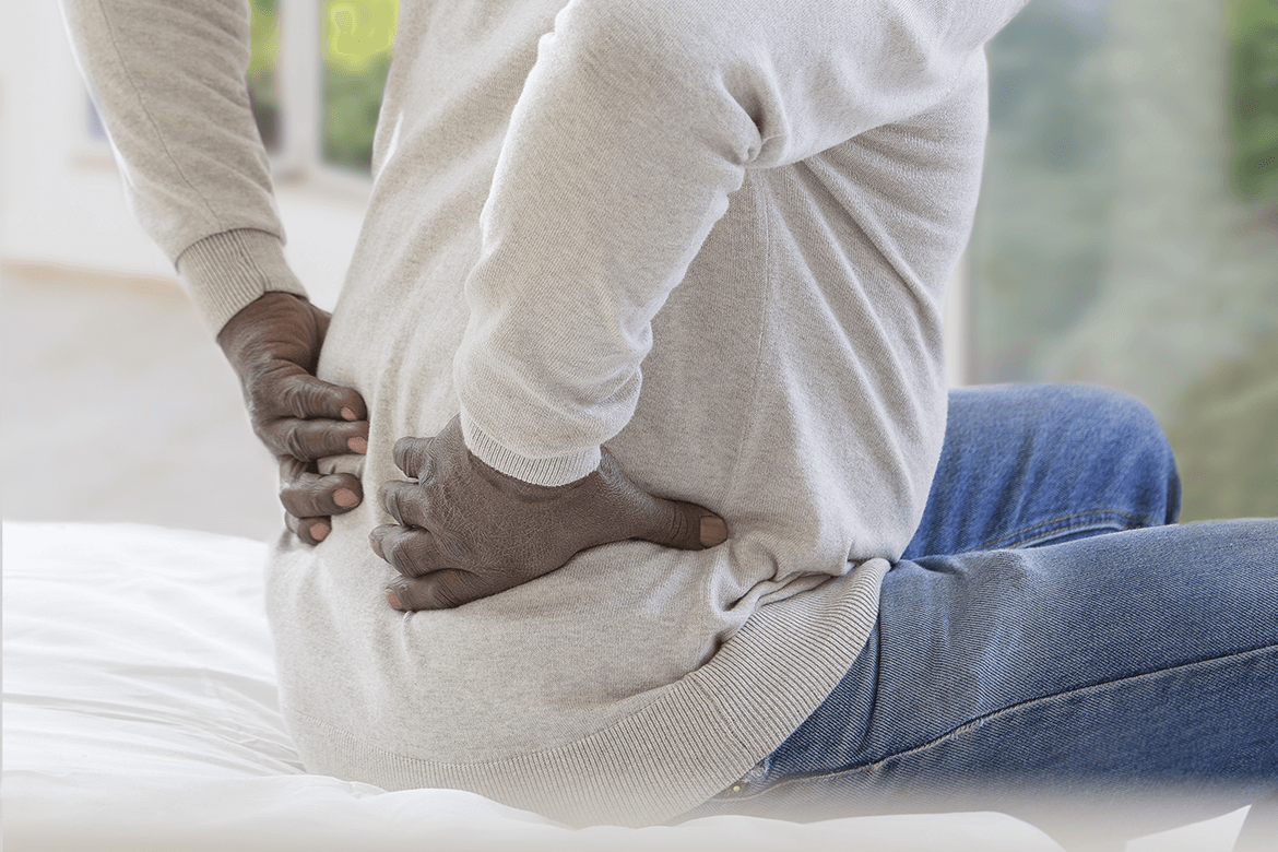 Man sitting on bed holding lower back in pain