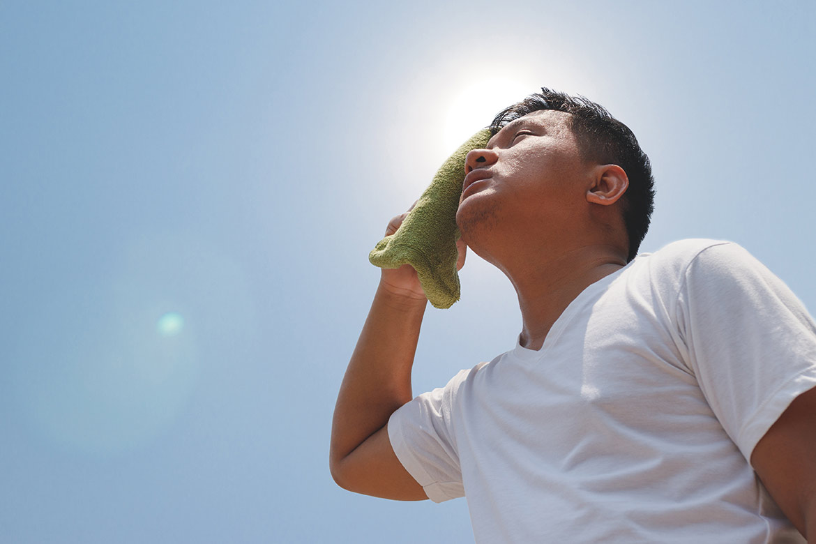 Man standing under sun wiping sweat from forehead