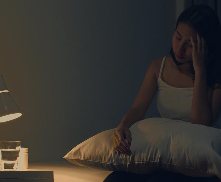 Woman in pain sitting on a bed in the dark 