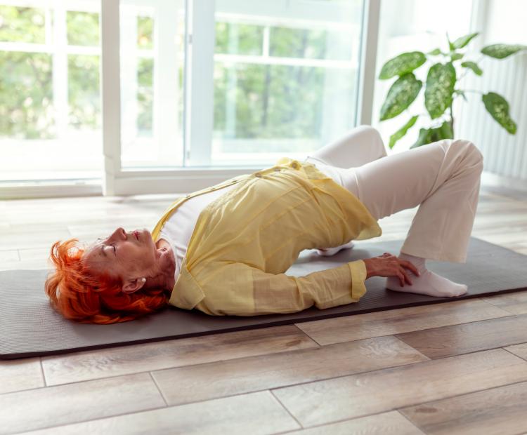 Elderly woman stretching on a floor mat.