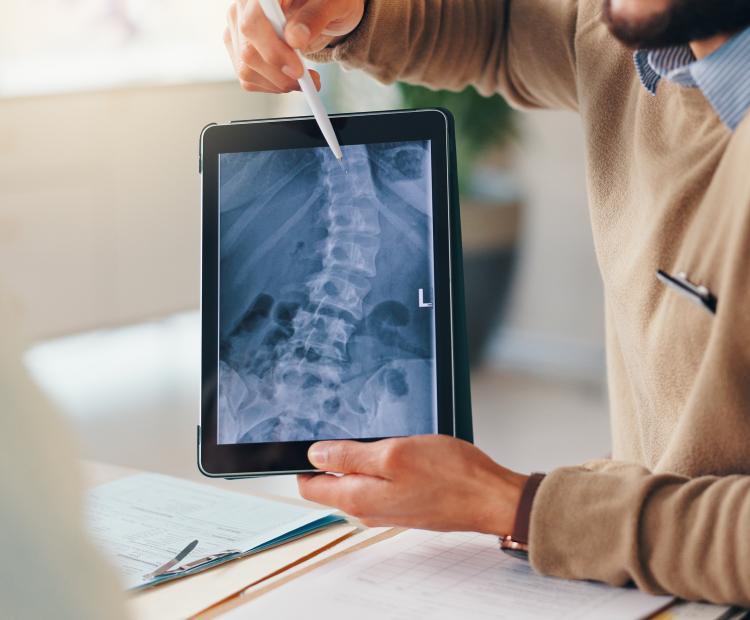 Doctors showing an x-ray of a curved spine to a patient on a tablet.