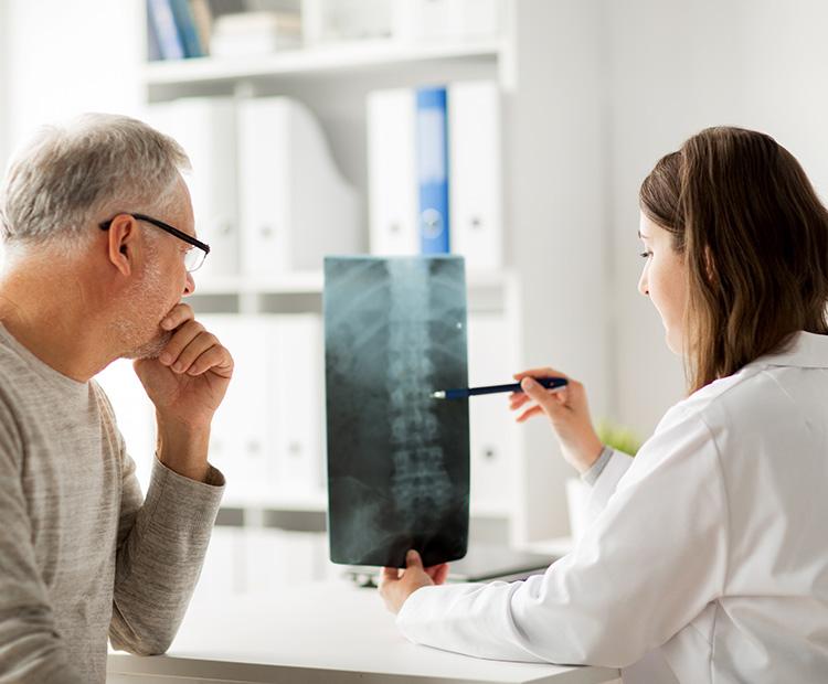 A patient sits with his doctor as she reviews his spinal xray