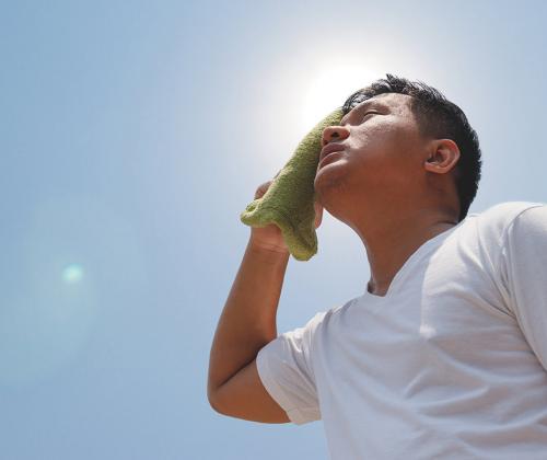 Man standing under sun wiping sweat from forehead