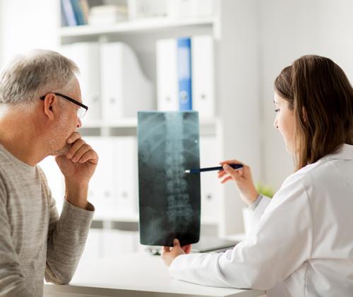 A patient sits with his doctor as she reviews his spinal xray