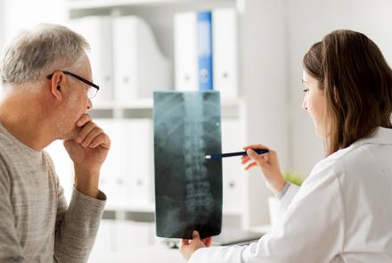 A patient sits with his doctor as she reviews his spinal xray